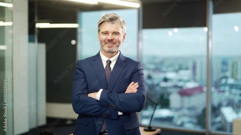 Portrait of a mature adult gray bearded businessman in a formal suit and tie looking at the camera in a modern glass office. Confident senior business man, entrepreneur in business with arms crossed Portrait of a mature adult gray bearded businessman in a formal suit and tie looking at the camera in a modern glass office. Confident senior business man, entrepreneur in business with arms crossed