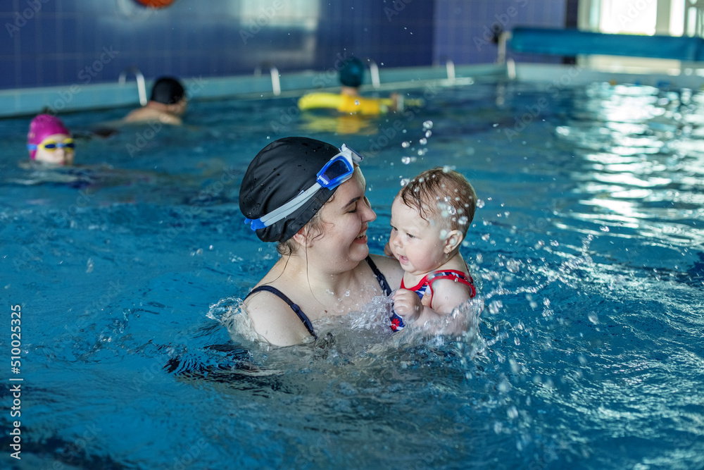 Smiling happy mother with baby girl in swimming pool. Sport, training and family concept.