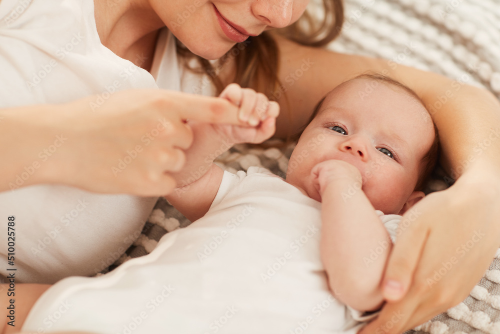 Smiling woman lying on bed with her little daughter sucking finger and looking at camera Smiling woman lying on bed with her little daughter sucking finger and looking at camera