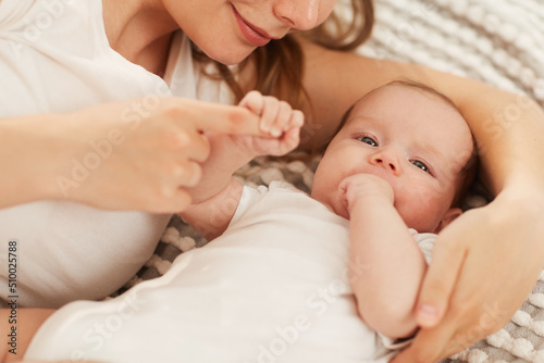 Smiling woman lying on bed with her little daughter sucking finger and looking at camera
