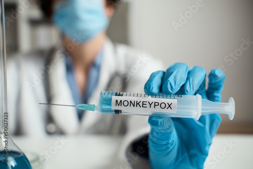 Doctor in mask, white coat holds syringe inscription Smallpox. Monkeypox is virus transmitted to humans from animals Symptoms similar to smallpox. Monkey includes variola, vaccinia, vaccinia viruses
 photo