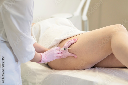The hands of a woman doctor cosmetologist in pink gloves holds a syringe and makes an injection of lipolytic into the thigh of a female patient for weight loss photo