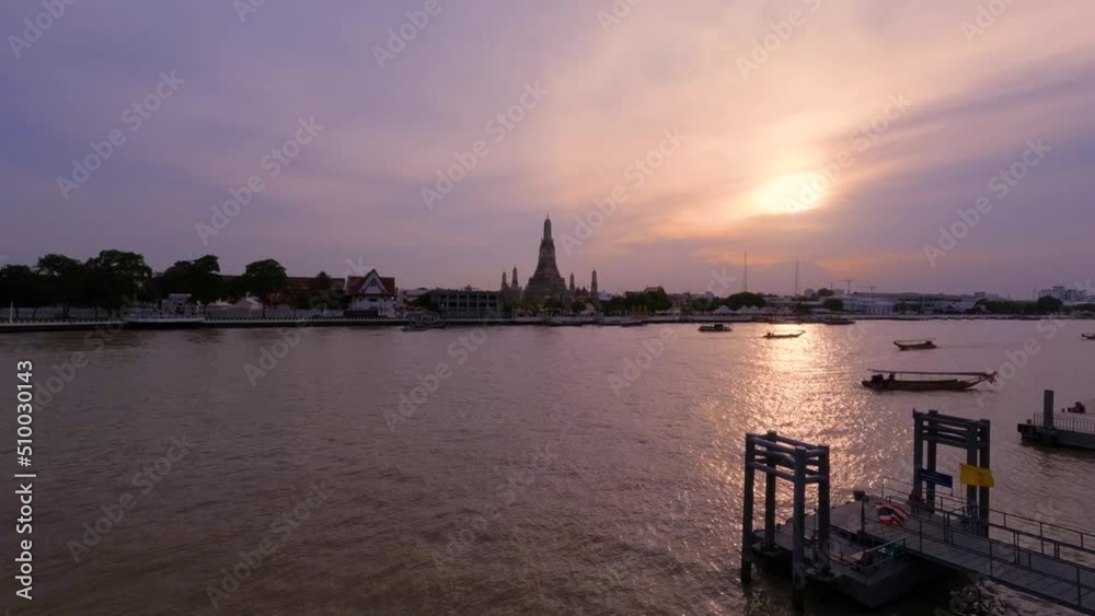 Travel Boats Cruising along Chao Phraya River with Wat Arun Temple in the background on Picturesque sunset in Bangkok - timelapse