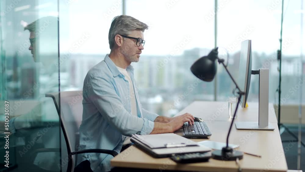 silhouette mature gray-haired confident business man in casual clothes working at pc computer workplace in a modern glass office at desk. Focused senior male bearded businessman, employee at work