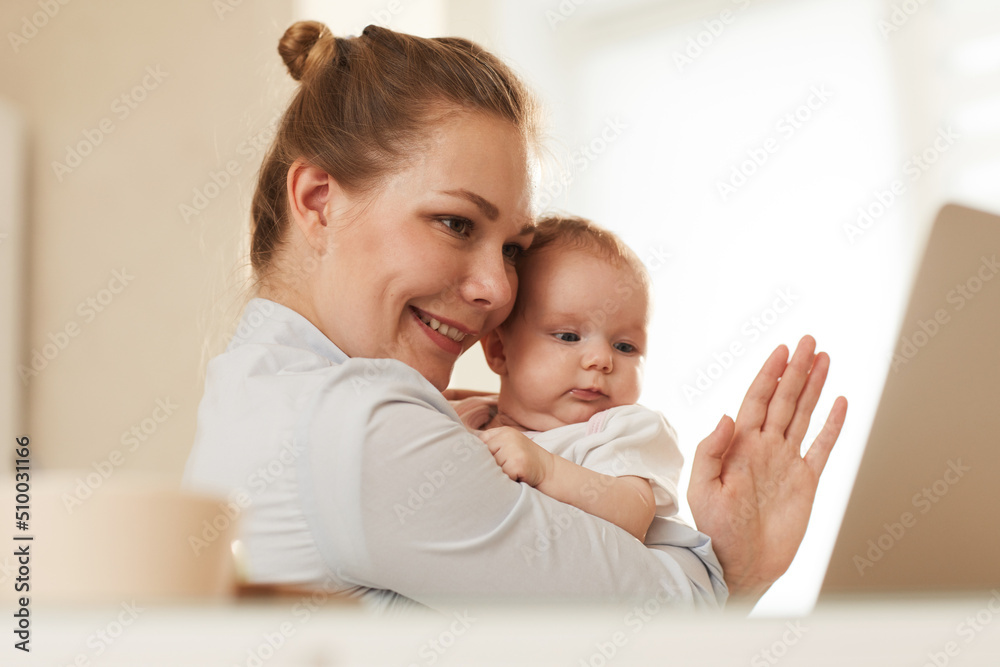 Young smiling mother showing her baby and waving to grandmother who is calling them through Skype Young smiling mother showing her baby and waving to grandmother who is calling them through Skype