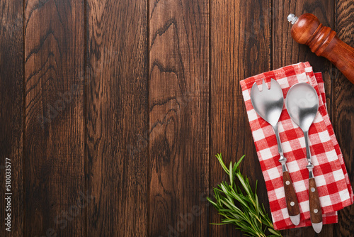 Food background. Salt, pepper, rosemary branch, wooden stand, salad fork and spoon, red napkin on wooden cooking background. Food cooking background. Ingredients for cooking food background. Mock up