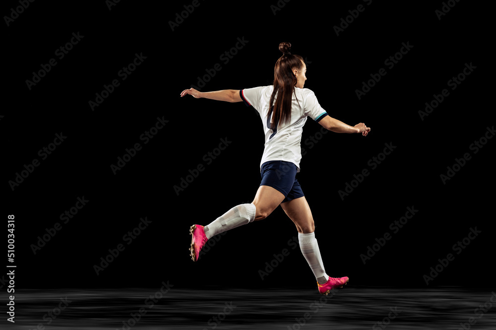 Back view of energetic soccer, football player running isolated on dark background. Sport, action, competitions, games and fitness concept