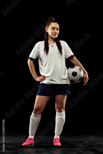 Full-length portrait of sportive girl, female soccer, football player posing isolated on black studio background. Sport, action, motion, fitness concept © master1305