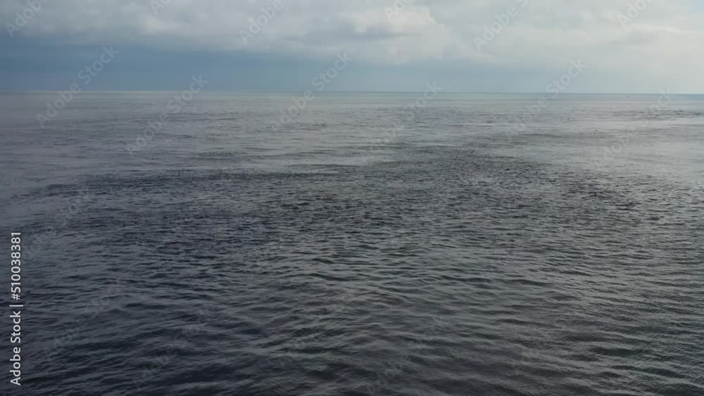 slow aerial of small ripples in the flat and calm ocean with storm on horizon slow aerial of small ripples in the flat and calm ocean with storm on horizon