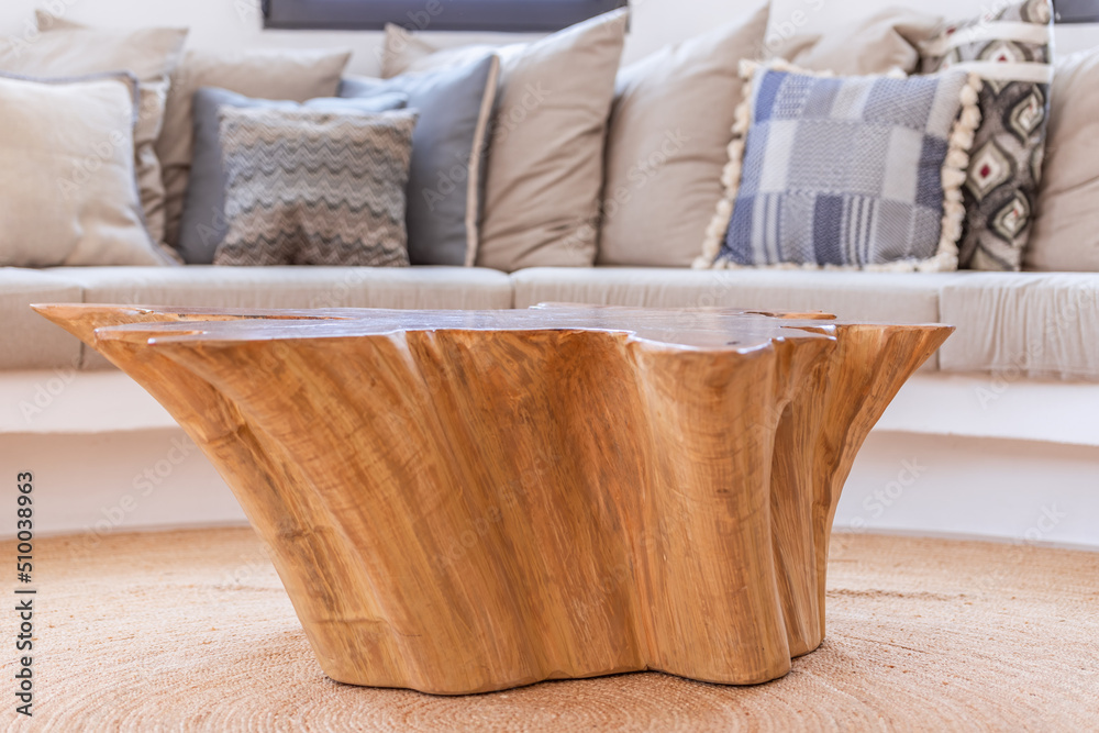 Coffee table made of a single solid natural wood surrounded by a sofa with countless cushions in the light living room of a Mediterranean villa Coffee table made of a single solid natural wood surrounded by a sofa with countless cushions in the light living room of a Mediterranean villa
