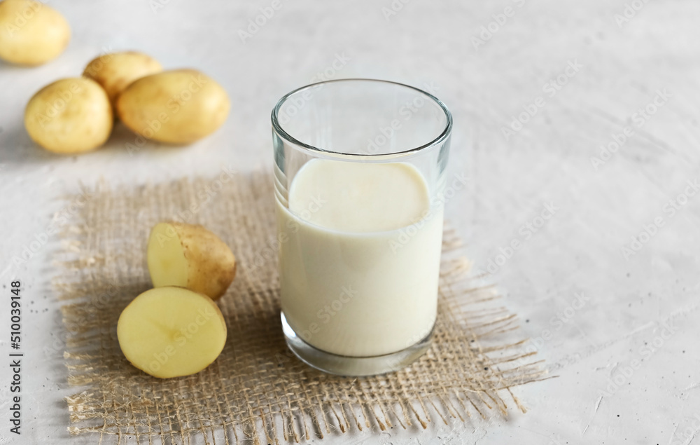 Vegan potato milk in a glass and potatoes on burlap on the wooden background, non-dairy alternative milk,  copy space. Potato milk contains many useful vitamins and minerals vitamin B6, vitamin C.