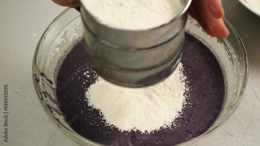Close-up of a baker sifting flour through a metal sieve into a glass bowl with black dye and cream. Top view. Concept of the bakery. Cake with his own hands Close-up of a baker sifting flour through a metal sieve into a glass bowl with black dye and cream. Top view. Concept of the bakery. Cake with his own hands