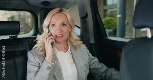 Attractive adult caucasian businesswoman in car talking on mobile phone. Female caucasian sitting on backseat of automobile and answer an iportant call. Freelance working concept photo