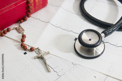 Flat lay of a cardiogram on which there is a crucifix, a stethoscope and a bible
