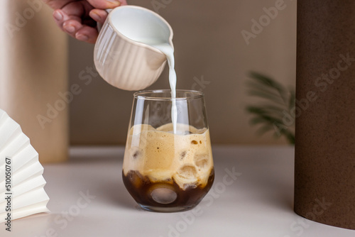Milk pouring into Iced coffee. Cold Coffee brew drink cocktail with ice cube on abstract background. Summer refreshing drink concept.