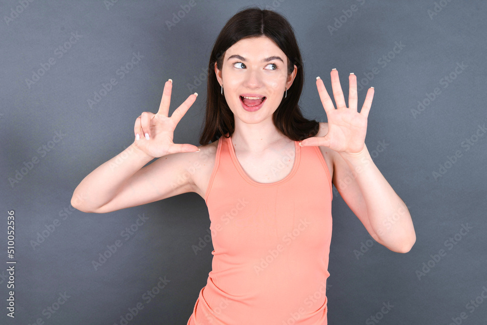 Caucasian woman wearing orange T-shirt over grey wall showing and pointing up with fingers number eight while smiling confident and happy. Caucasian woman wearing orange T-shirt over grey wall showing and pointing up with fingers number eight while smiling confident and happy.