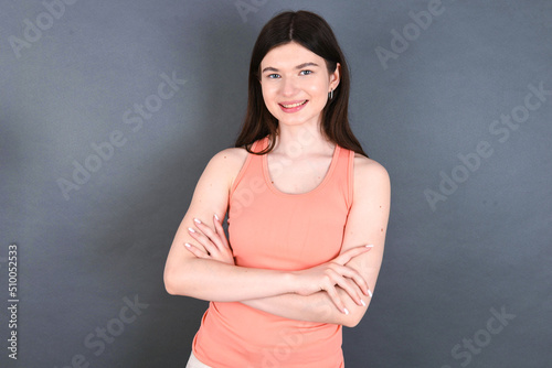 Caucasian woman wearing orange T-shirt over grey wall happy face smiling with crossed arms looking at the camera. Positive person.