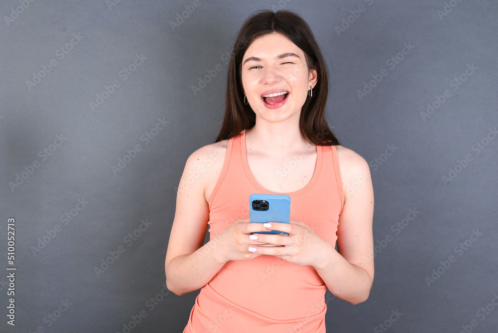 young beautiful Caucasian woman wearing orange T-shirt over grey wall taking a selfie celebrating success young beautiful Caucasian woman wearing orange T-shirt over grey wall taking a selfie celebrating success