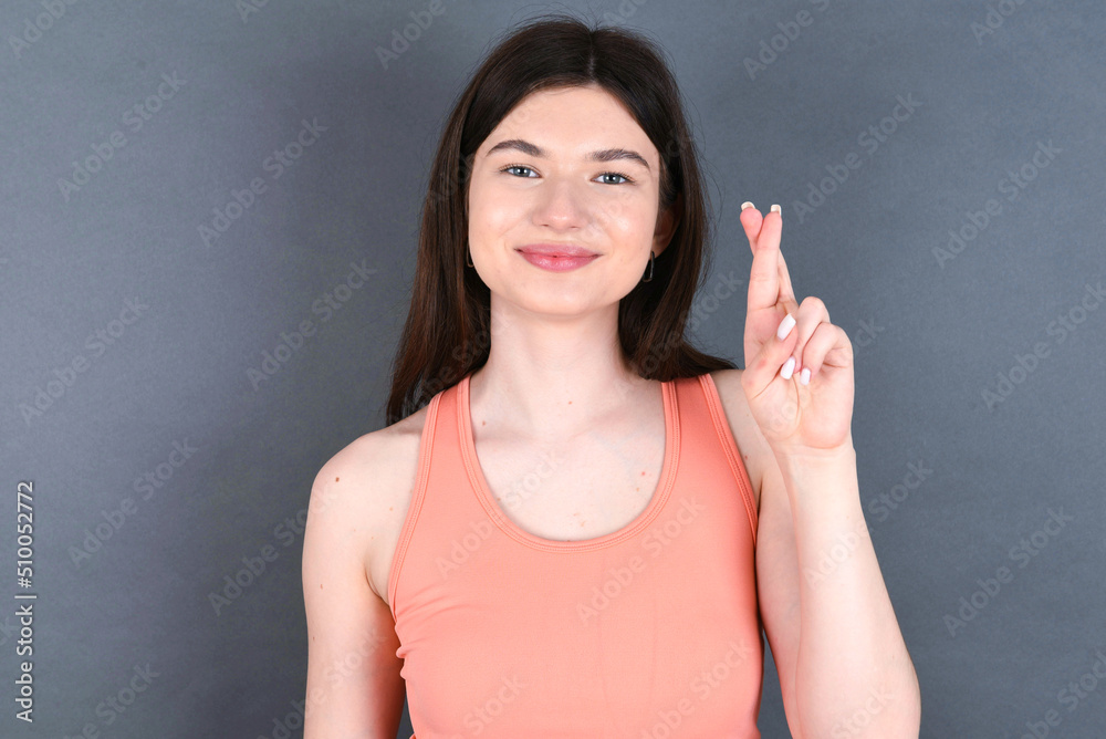 Fototapeta premium young beautiful Caucasian woman wearing orange T-shirt over grey wall pointing up with fingers number ten in Chinese sign language Shi