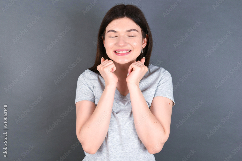 young beautiful Caucasian woman wearing white T-shirt over grey wall grins joyfully, imagines something pleasant, copy space. Pleasant emotions concept. young beautiful Caucasian woman wearing white T-shirt over grey wall grins joyfully, imagines something pleasant, copy space. Pleasant emotions concept.