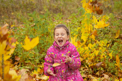 happy girl tosses leaves in the park in autumn