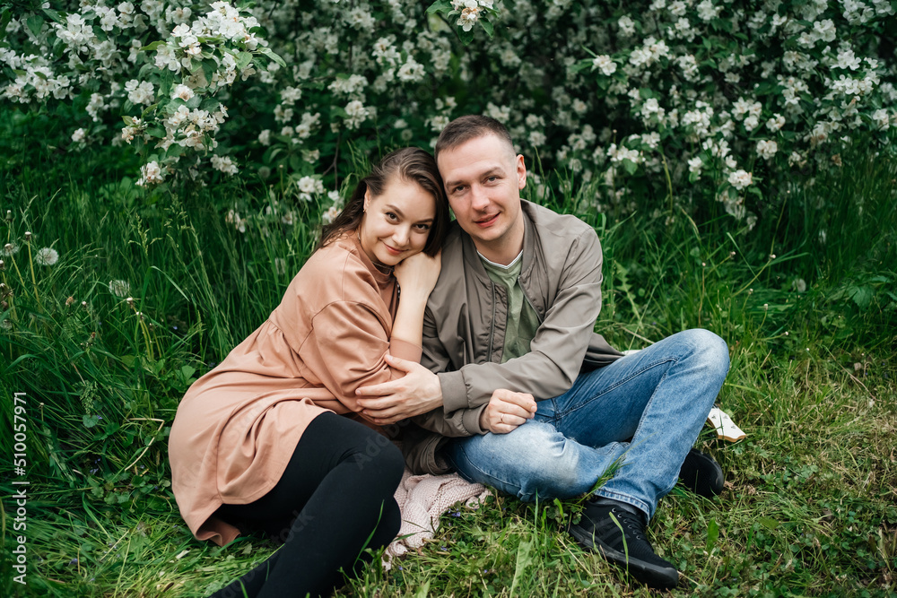 young couple in love a girl and a man sit on the grass of a flowering apple tree the aroma of flowers outdoors young couple in love a girl and a man sit on the grass of a flowering apple tree the aroma of flowers outdoors