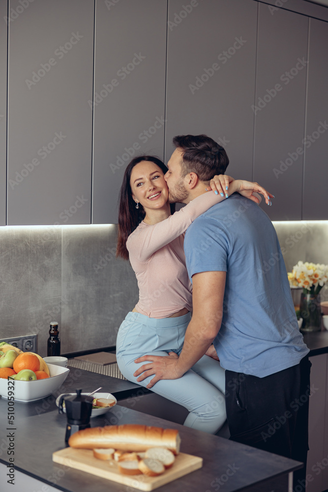 Caucasian handsome man kissing beauiful woman ,couple standing in kitchen in morning.
