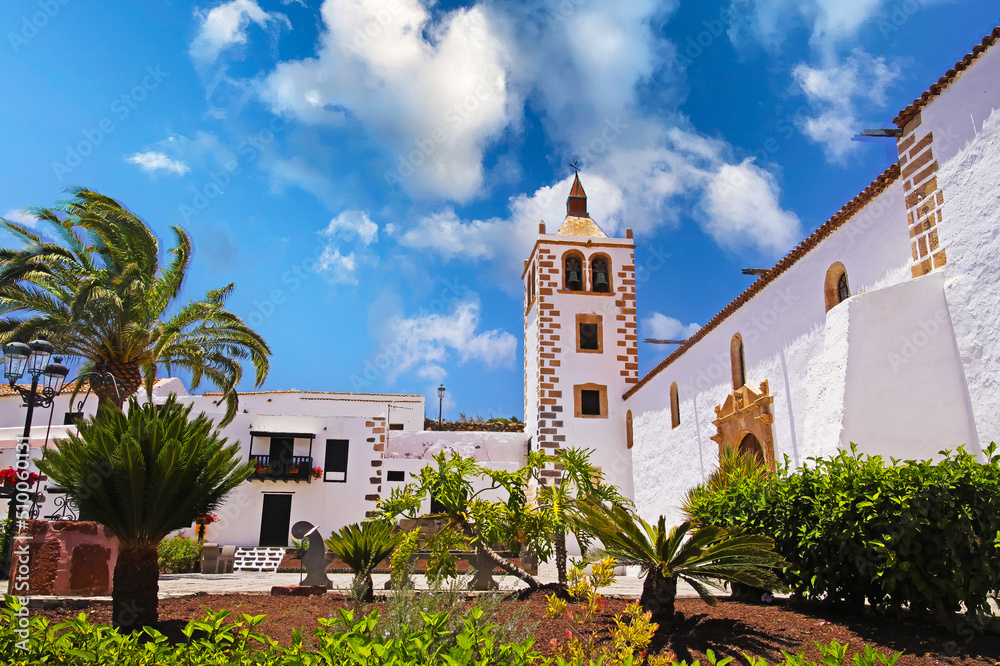 Beautiful colonial canary island  style typical traditional church, white houses, bell tower, garden, palm tree, blue summer sky - Betancuria, Fuerteventura -
