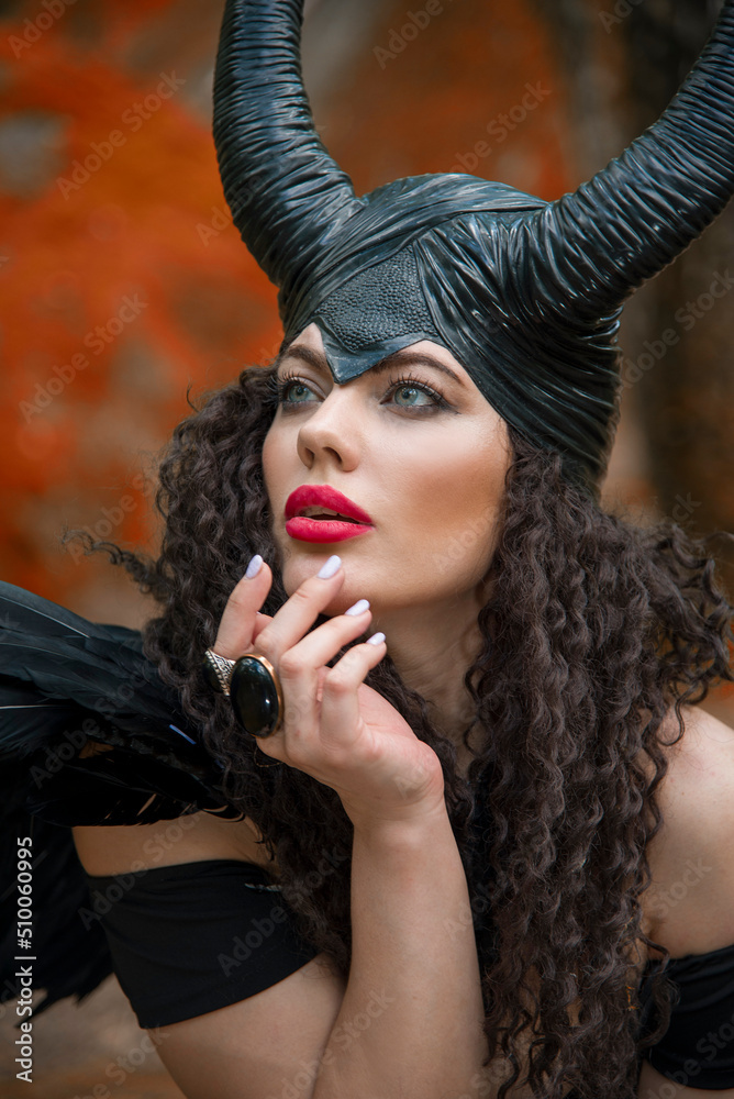 Concept of Halloween and fantasy horror. Cosplay on Maleficent demonic - starring. Face of beautiful woman from a fairytale in autumn forest. Beautiful girl dressed up as devil