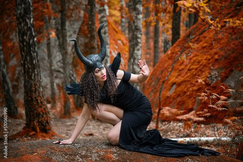 Concept of Halloween and fantasy horror. Cosplay on Maleficent demonic - starring. Face of beautiful woman from a fairytale in autumn forest. Beautiful girl dressed up as devil photo