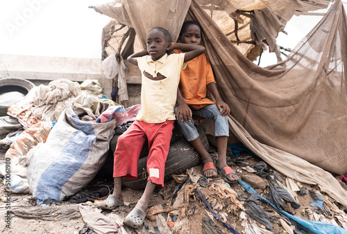 фотографія Two young desperate African children sitting on tires and waste on a huge garbage dump in a village near Bamako, in Mali (Africa)