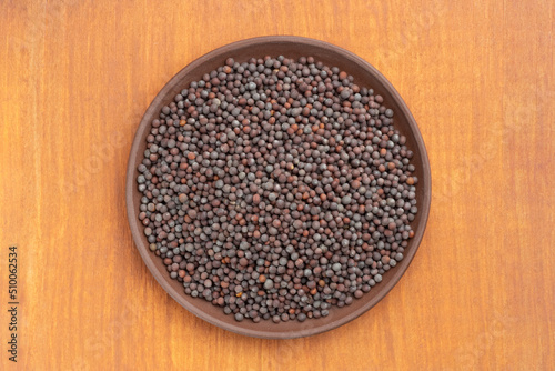 Spice Mustard seeds (Brassica juncea) in brown clay plate on brown wooden background. Close up. Healthy eating concept
