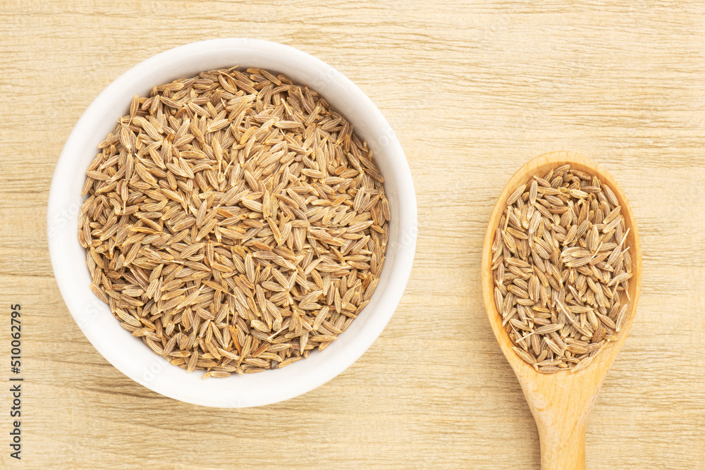 Spice cumin (jeera) in white ceramic bowl and spoon on brown wooden background. Vegetarian food concept