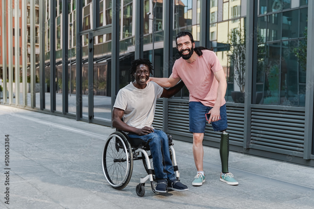 Multiracial friends with disability having fun looking at camera outdoor - Focus on African man sitting on wheelchair Multiracial friends with disability having fun looking at camera outdoor - Focus on African man sitting on wheelchair
