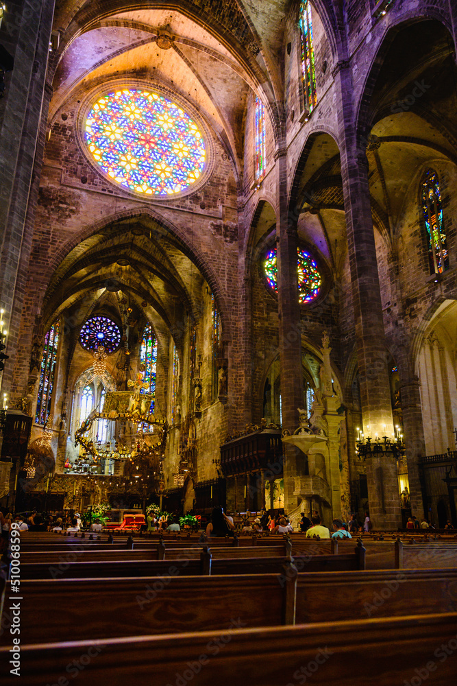 Vertical photograph of the rose window in the foreground of the pews inside the cathedral of Mallorca