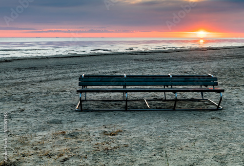 Resting bench on sandy beach of the Baltic Sea during colorful sunrise