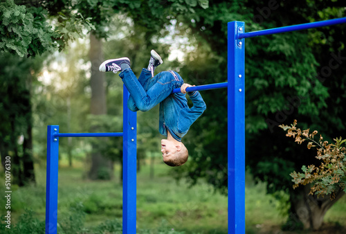 boy is playing on playground  hanging upside down on a horizontal bar 