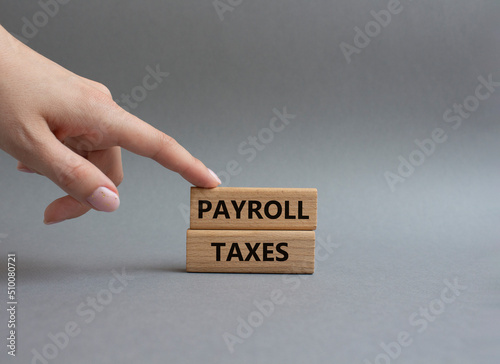 Payroll taxes symbol. Concept word Payroll taxes on wooden blocks. Beautiful grey background. Businessman hand. Business and Payroll taxes concept. Copy space.