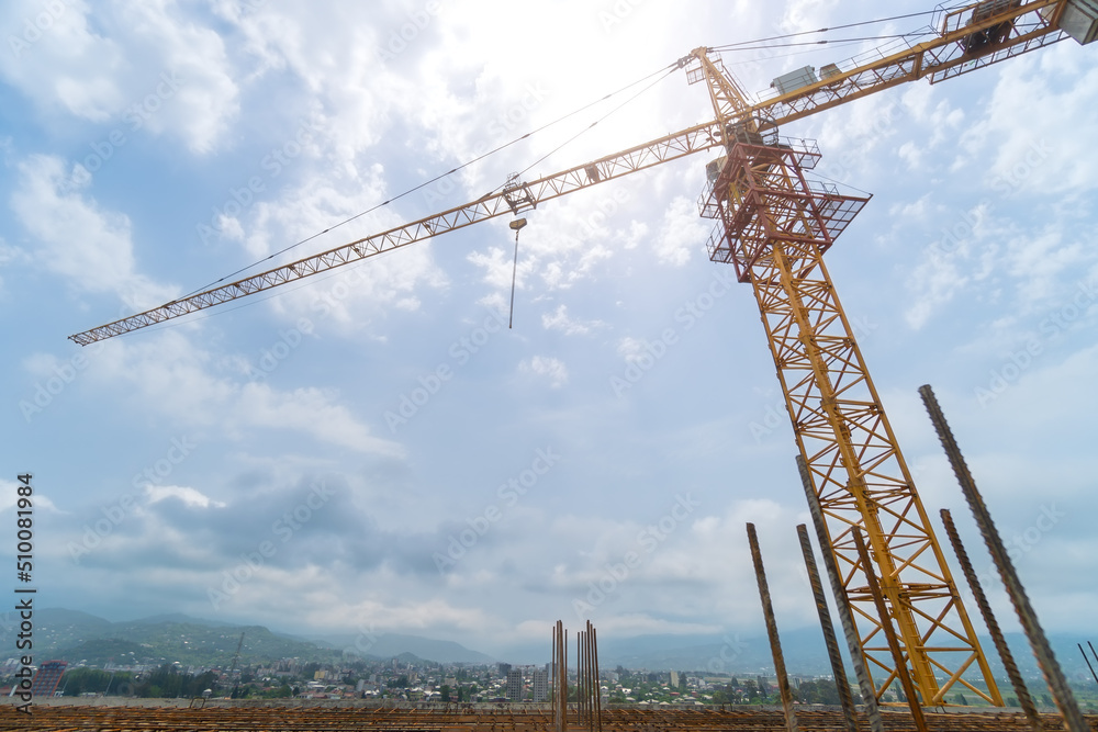 Close-up of a construction crane on a construction site with protruding fittings for screed against the background of mountains and cloudy sky