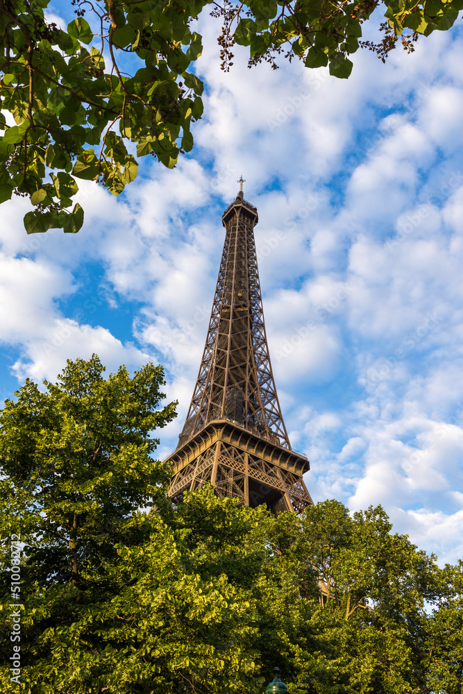 Partie supérieure de la Tour Eiffel devant un ciel partiellement nuagueux