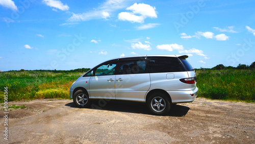Silver modern minivan. Japanese car. Located in nature. Sunny day. Blue sky. Travel by car. Family transport. Side view. photo