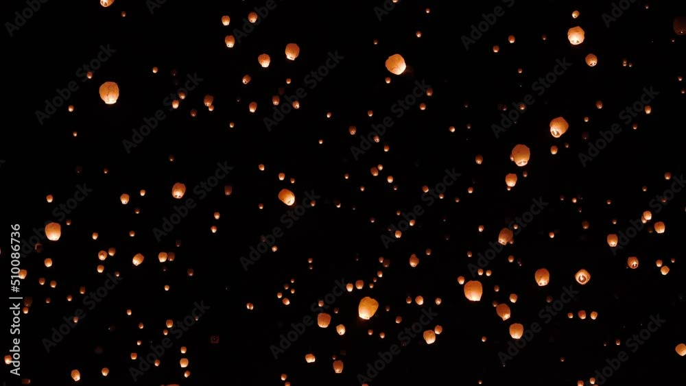 View of sky lanterns floating up through the sky at night during celebration event.
