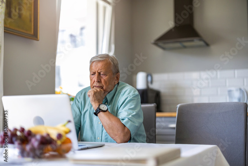 Elderly man using laptop at kitchen table 