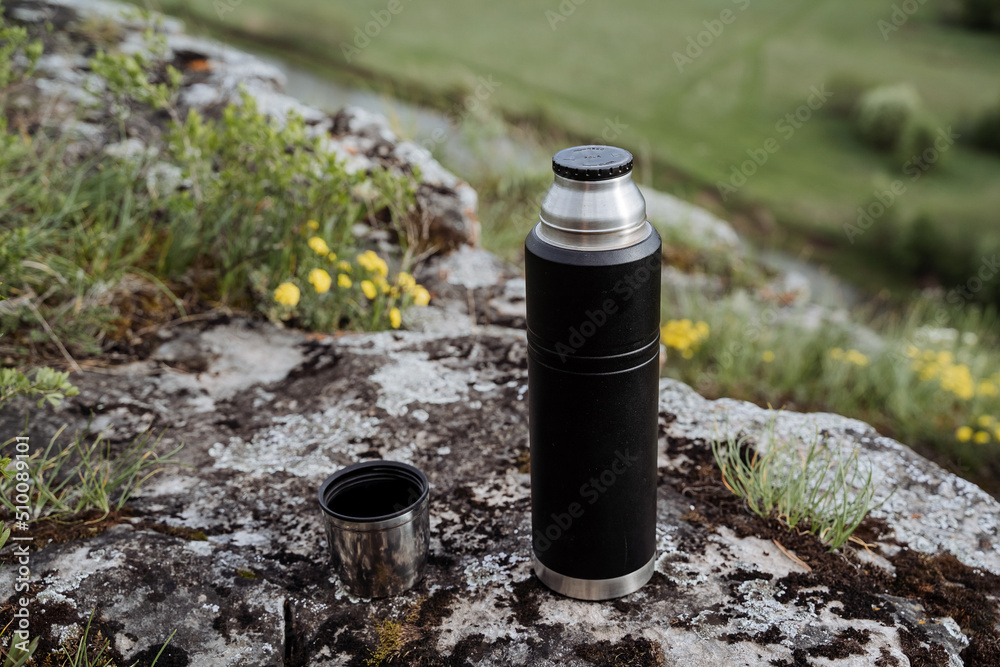 Drink tea in nature from a thermos, open lid, pour tea into a mug, hike in the mountains, camping in nature, tourist dishes, thermo bottle. Drink tea in nature from a thermos, open lid, pour tea into a mug, hike in the mountains, camping in nature, tourist dishes, thermo bottle.