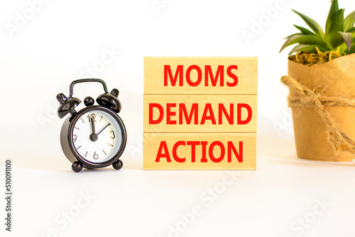 Moms demand action symbol. Concept words Moms demand action on wooden blocks on a beautiful white table white background. Black alarm clock. Business, finacial and Moms demand action concept. photo