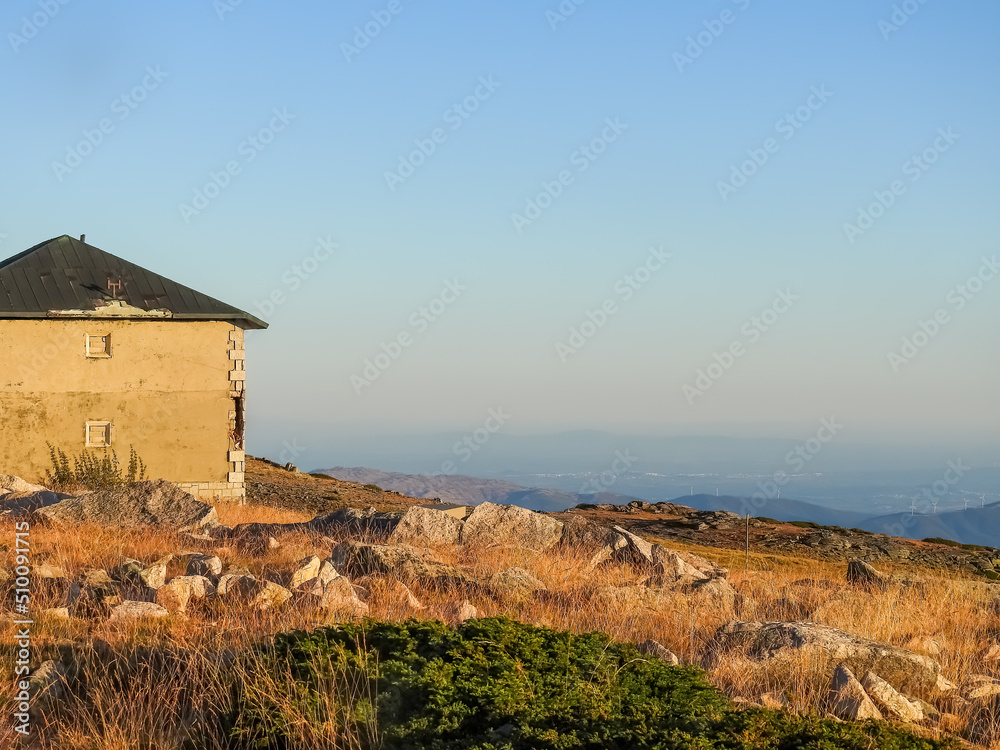 Mountain landscape at Torre, Serra da Estrela, Portugal. Orange sunset at  the mountain chain and built structure. Mists among the mountains.