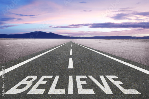 Believe text written on a highway at the beach with the sunset in the background for belief or faith concept.