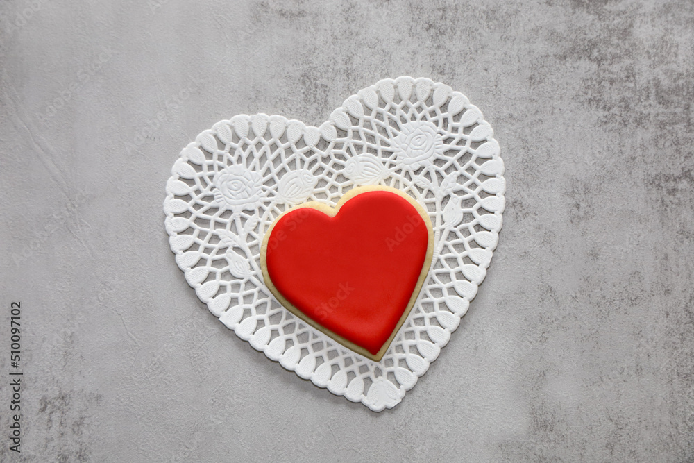 Backdrop with heart shaped sugar cookie with royal icing on top of a white doily with copy space. Backdrop with heart shaped sugar cookie with royal icing on top of a white doily with copy space.