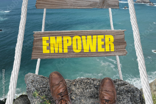 The word Empower on a challenging bridge above the ocean.