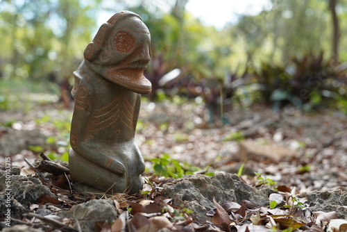 Taino Antique Stone Cemi Idol God Figure standing over rocks on the ground, close up. Taino Mythology. photo